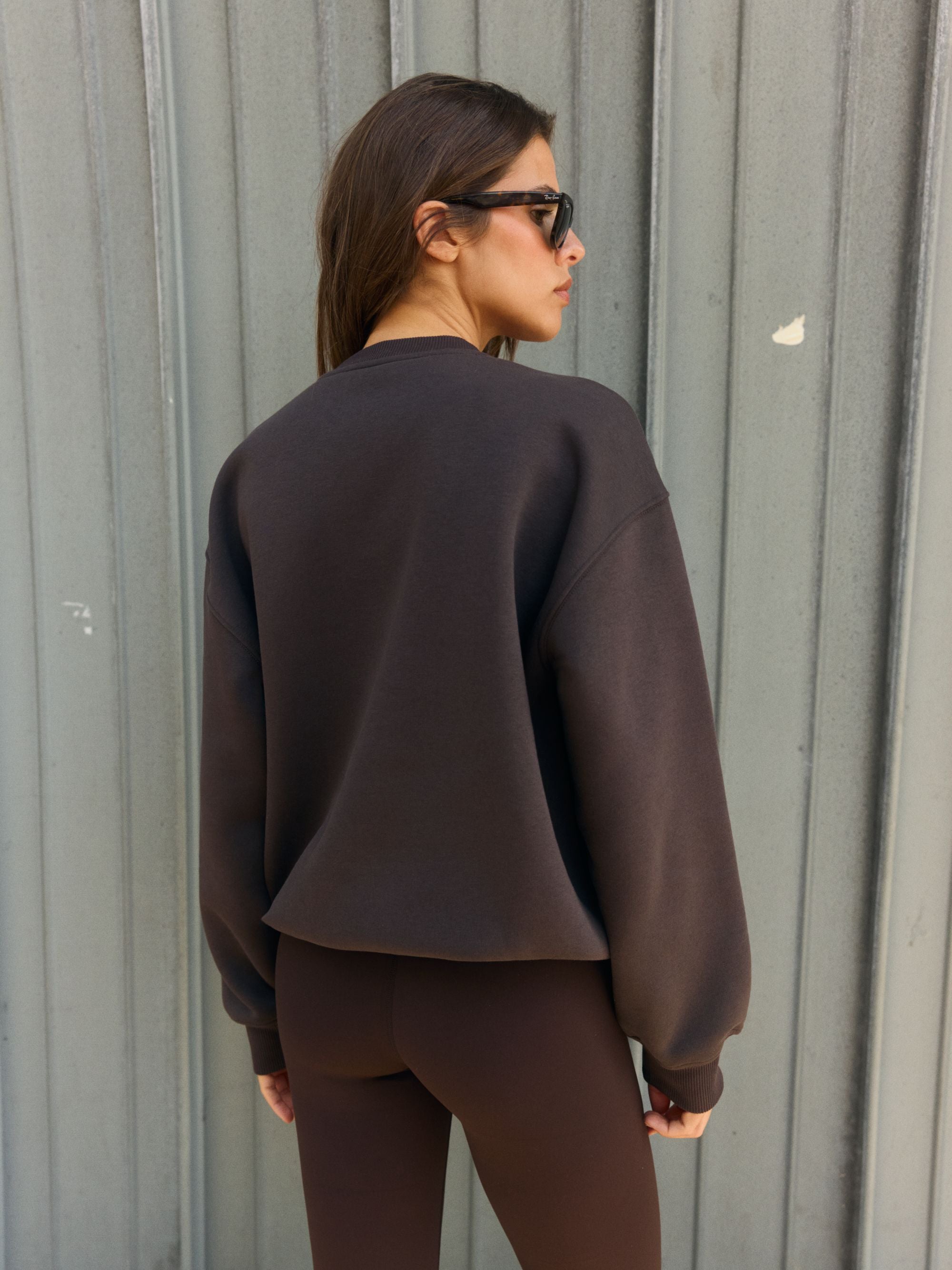 Woman wearing an oversized espresso brown CASPARA crewneck sweatshirt, seen from behind.
